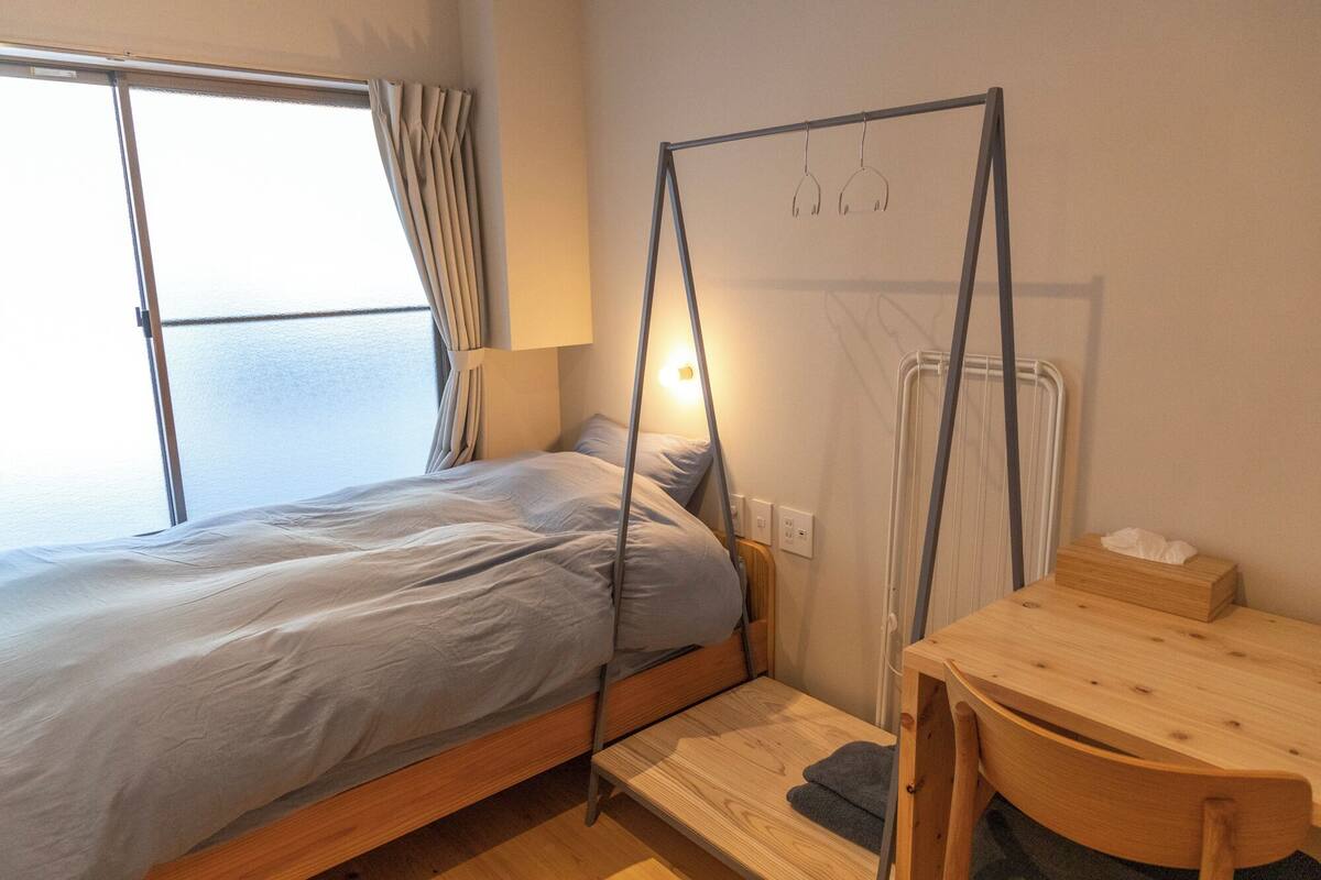 A single bed with a wooden frame, a bedside table, a lamp, and a window with curtains.