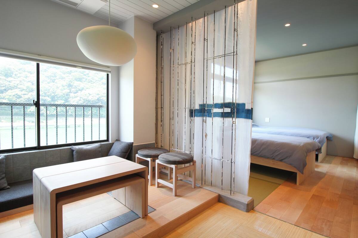 A modern bedroom with a bed, a seating area with a table, and a view through a large window.