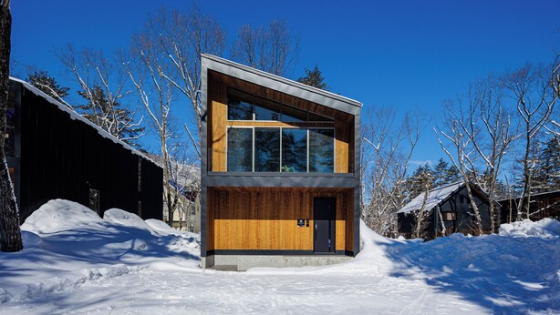 A modern two-story building with large windows, a wooden facade, and a snow-covered ground. - Credence Chalets (Hakuba)