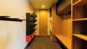 A hallway with a washing machine, a door, and a shelf with items on it. - Credence Chalets (Hakuba)
