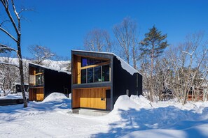 A modern building with large windows and a wooden facade, surrounded by snow and trees. - Credence Chalets (Hakuba)