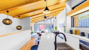 A modern kitchen with a wooden ceiling, pendant lights, a marble countertop, and a built-in oven. - Credence Chalets (Hakuba)