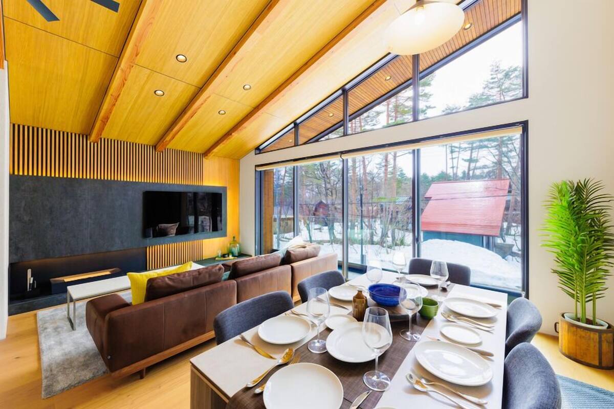 A modern dining area with a wooden ceiling, large windows, and a cozy seating arrangement.