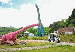 Una estatua de dinosaurio, un vehículo pequeño y un edificio en un entorno natural.