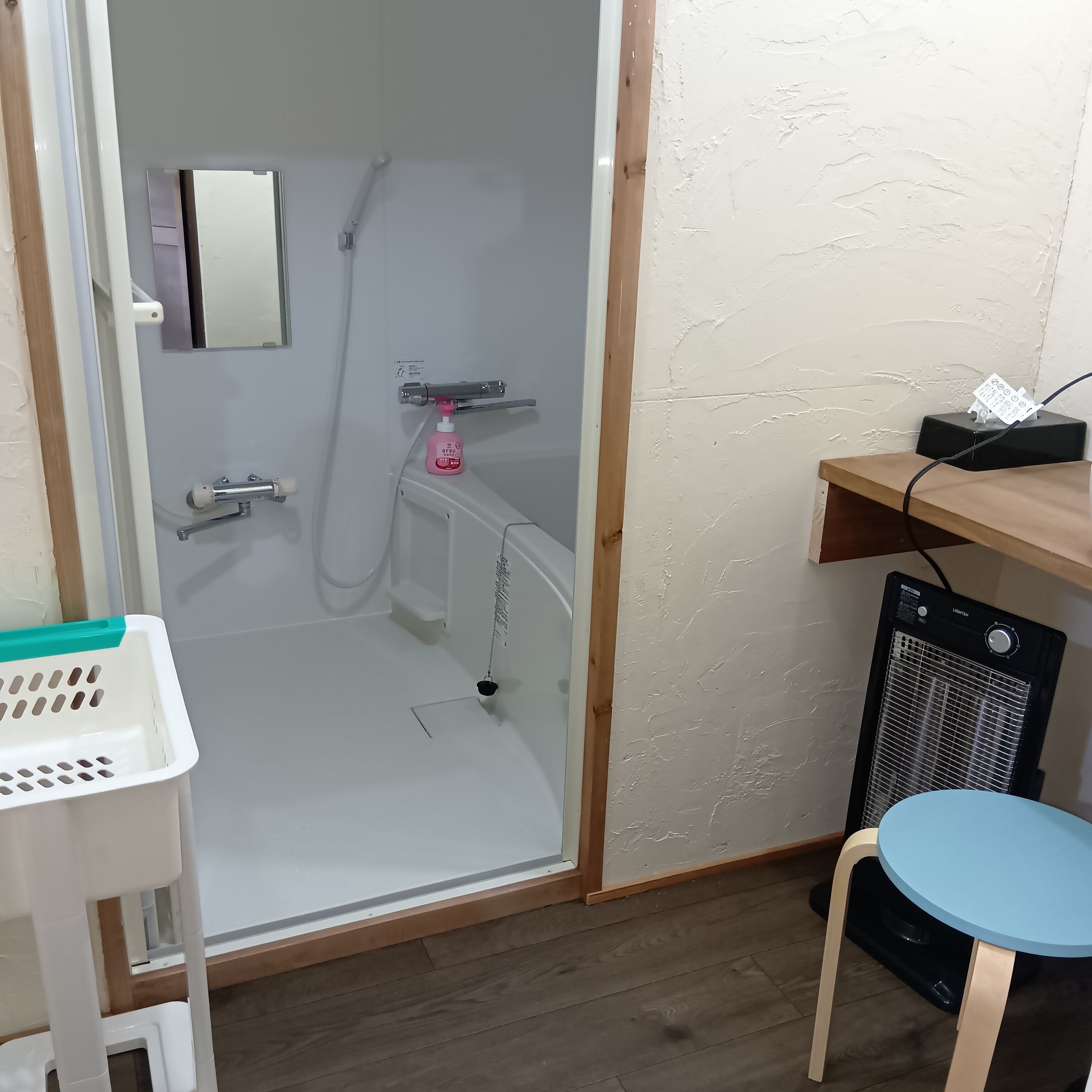 A shower area with a glass door, a white sink, a blue stool, and a heater on the floor.