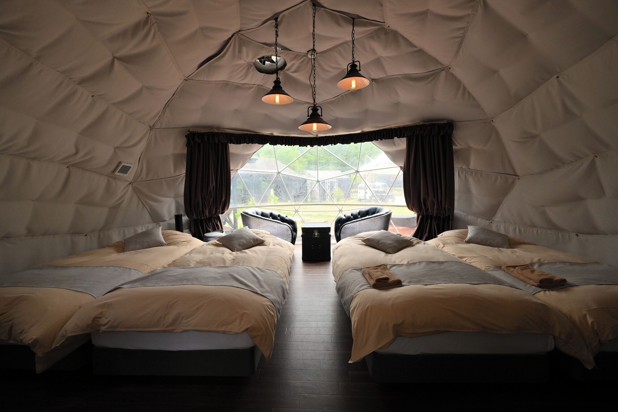 A tent-style room with two beds, a table, and hanging lights.