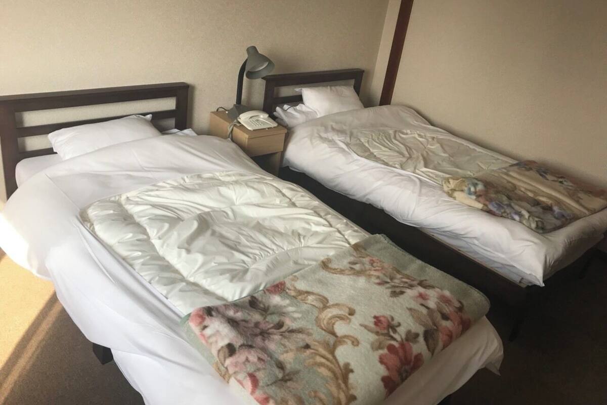 Twee enkele bedden met witte lakens, een nachtkastje met een lamp en een telefoon.