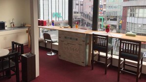 Een klein kantoor met een bureau, stoelen, een raam met uitzicht op gebouwen en een kitchenette.
