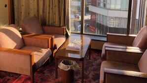 Een hotelkamer met een bank, fauteuils, een bijzettafeltje en een groot raam met uitzicht op de stad.