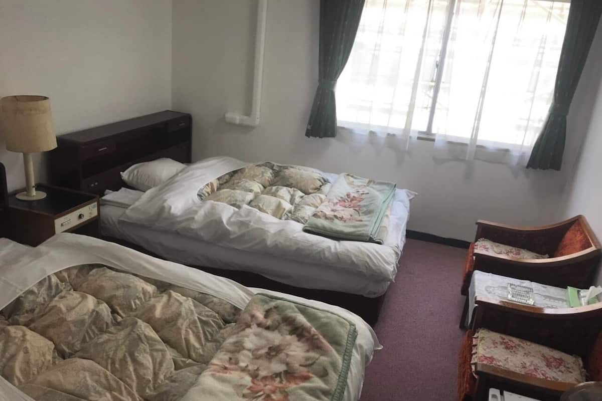 Een hotelkamer met twee bedden, een klein bureau en een stoel.
