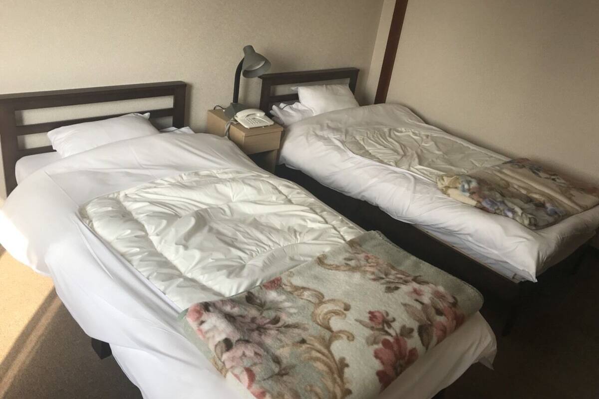 Twee enkele bedden met witte lakens, een nachtkastje met een lamp en een telefoon.