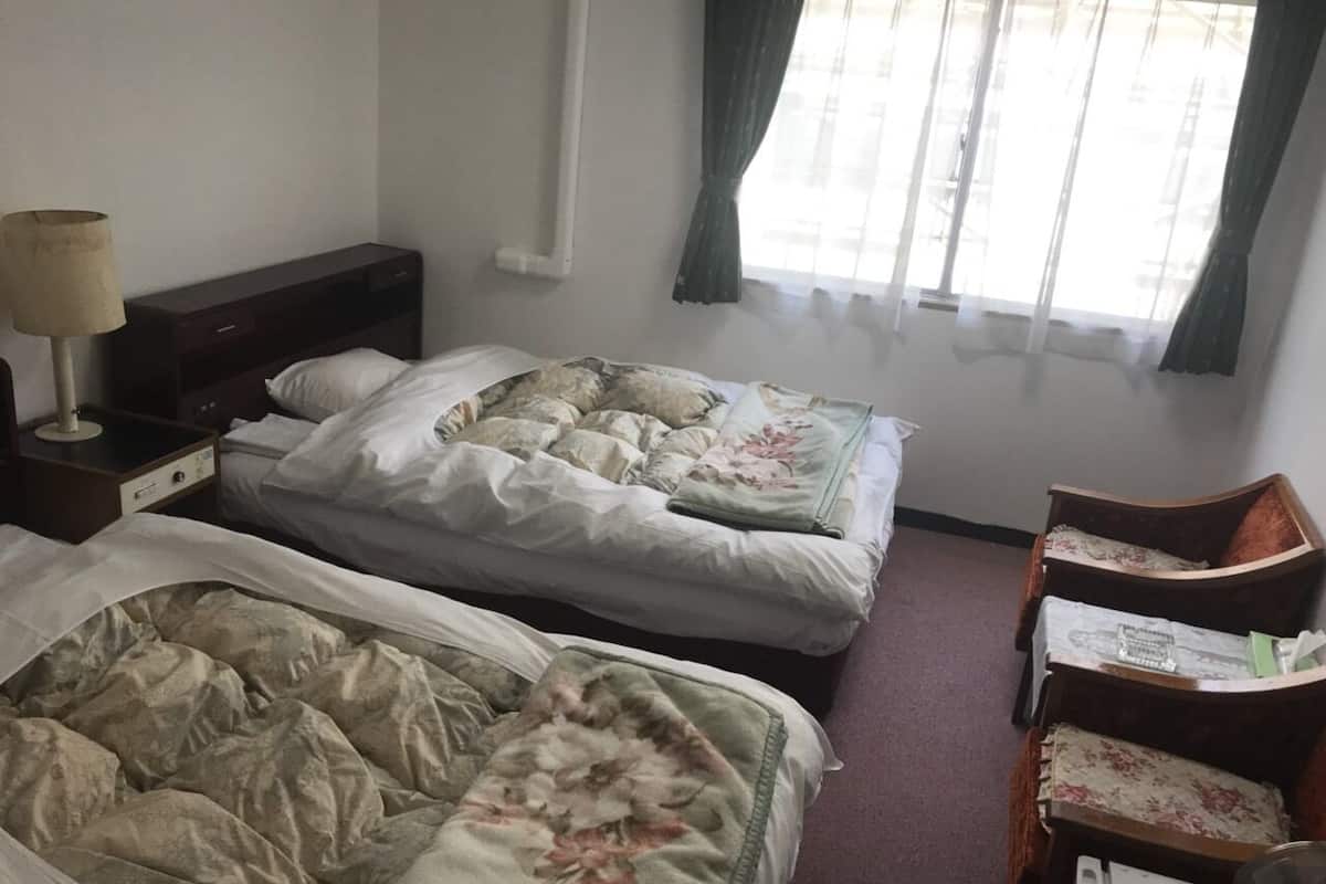 Een kamer met twee bedden, een nachtkastje, een stoel en een raam met gordijnen.