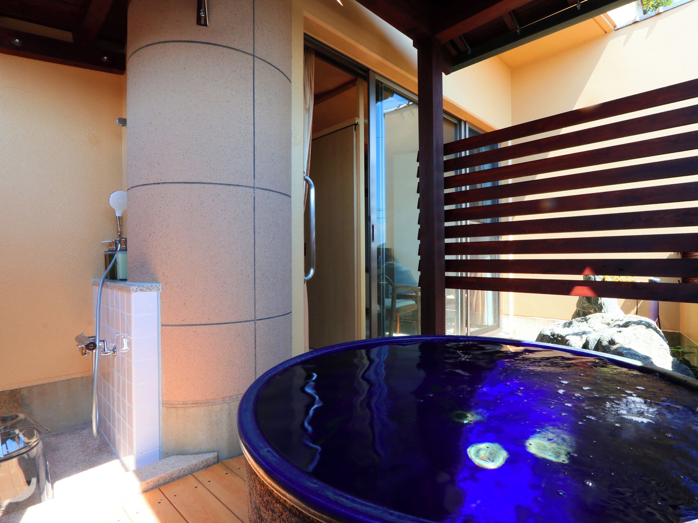 A hot tub with a wooden deck, a glass door, and a stone pillar.