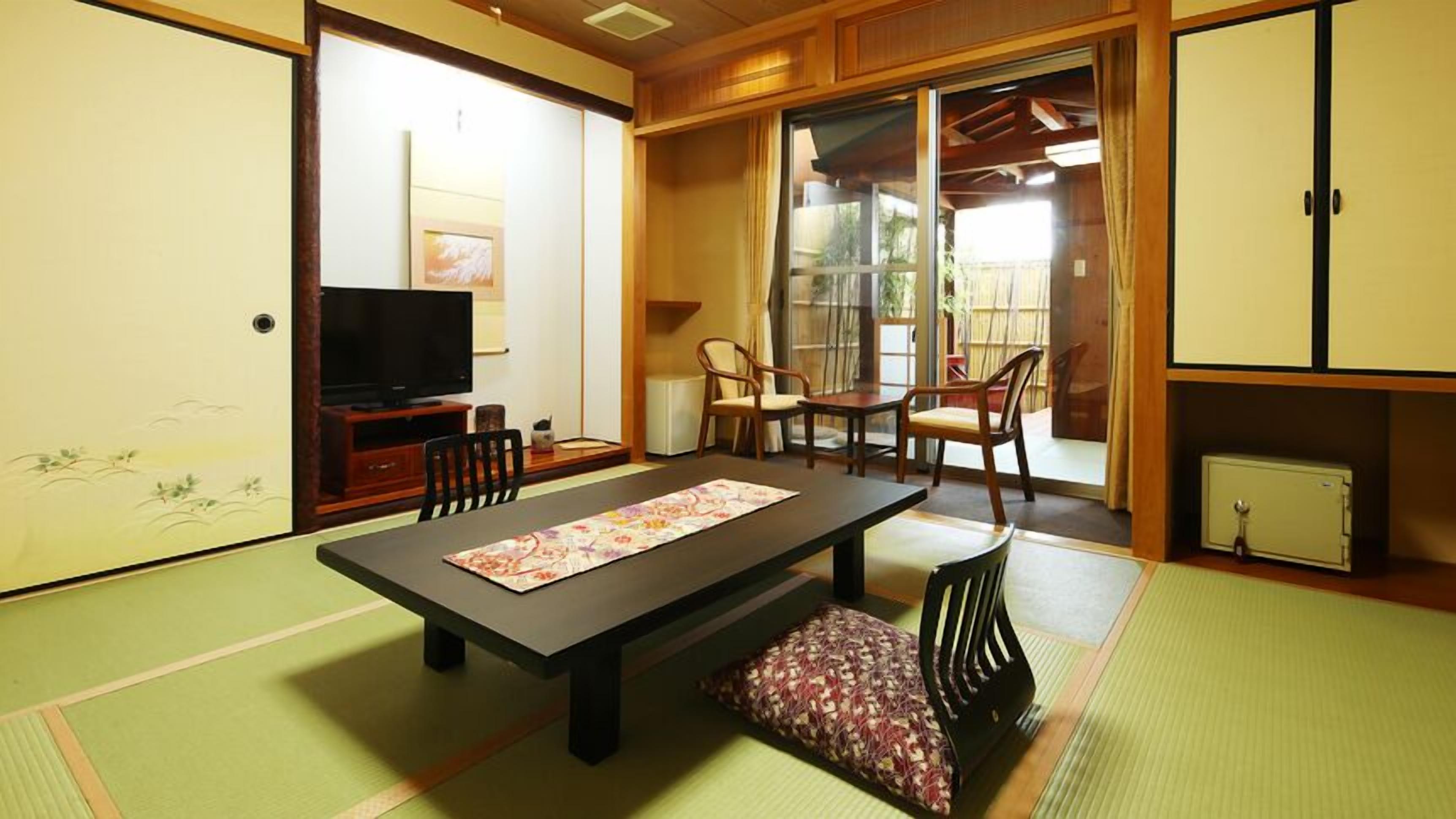 A traditional Japanese room with tatami flooring, a low table, chairs, a television, and sliding doors.