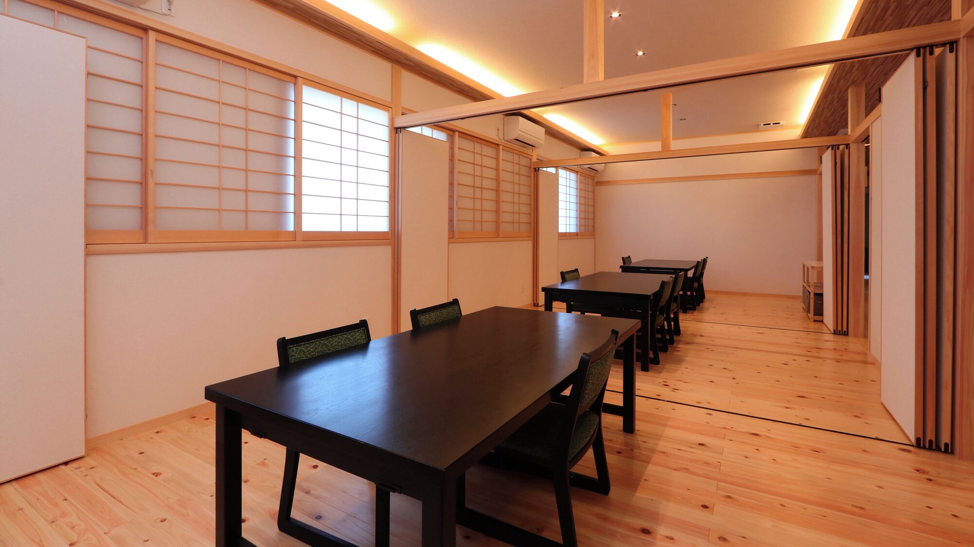 A conference room with a long table and chairs, wooden flooring, and shoji screens.