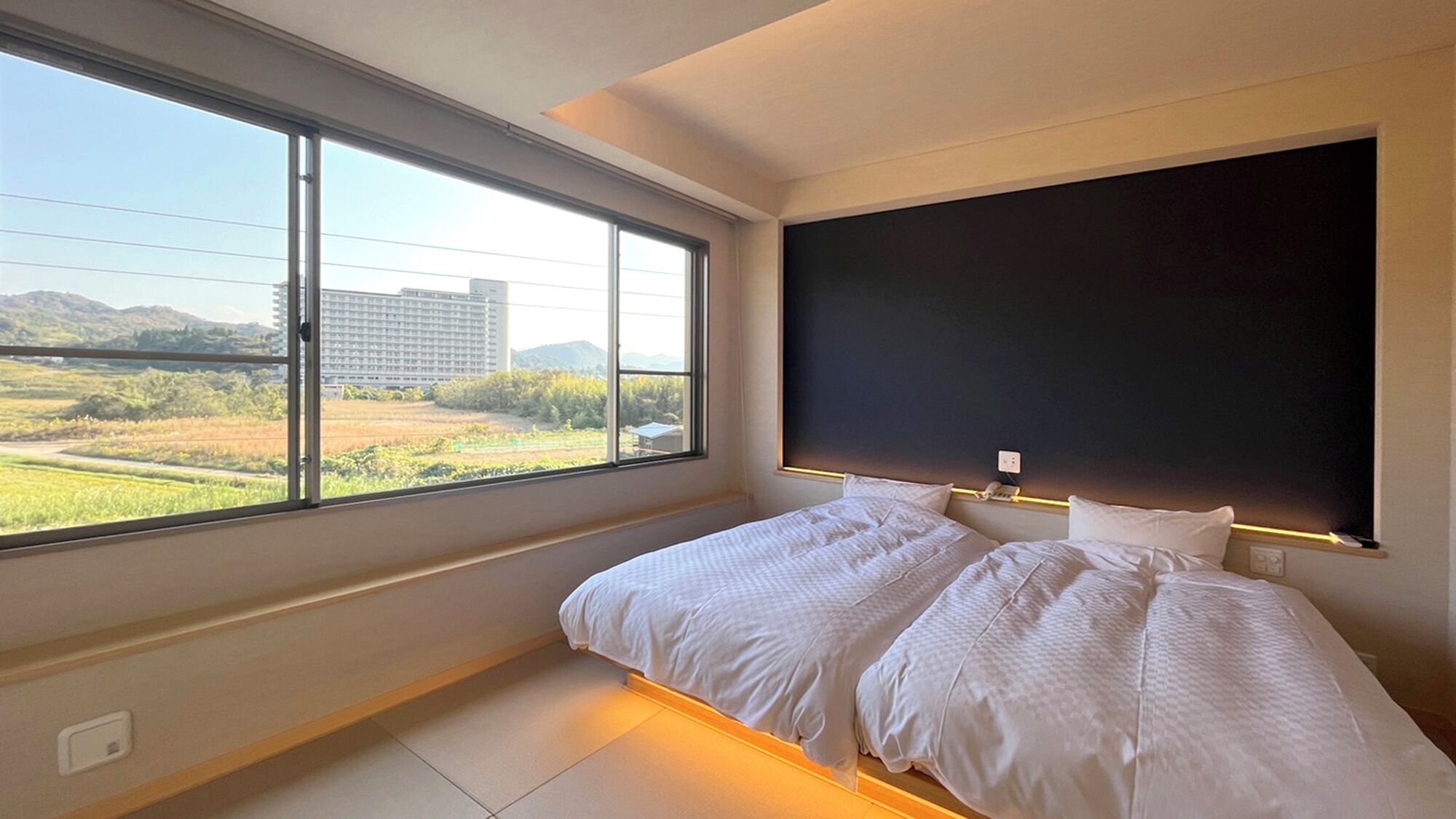 A bedroom with two beds, a large window, and a view of a building and landscape.