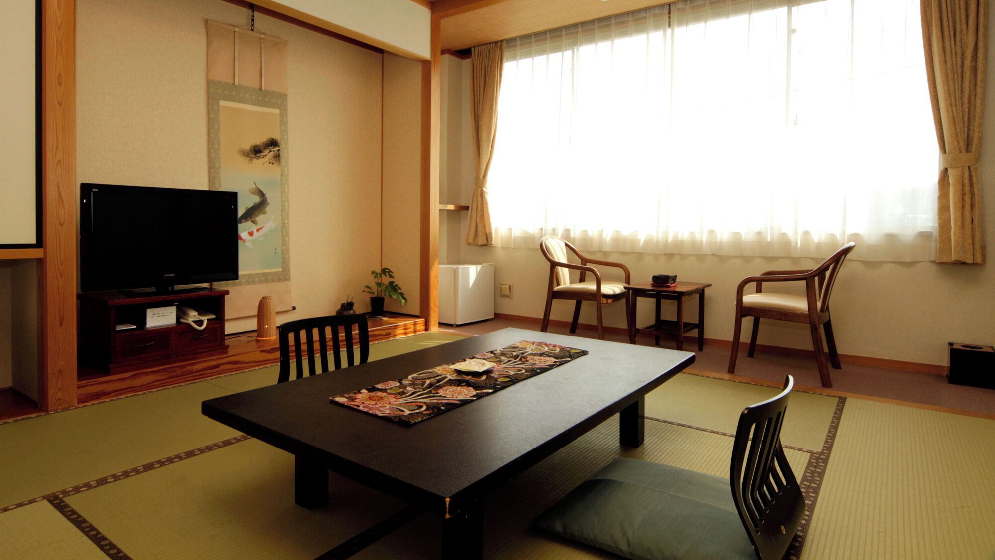 A traditional Japanese-style living room with tatami flooring, a low table with a decorative mat, a television, and a sliding door leading to another room.