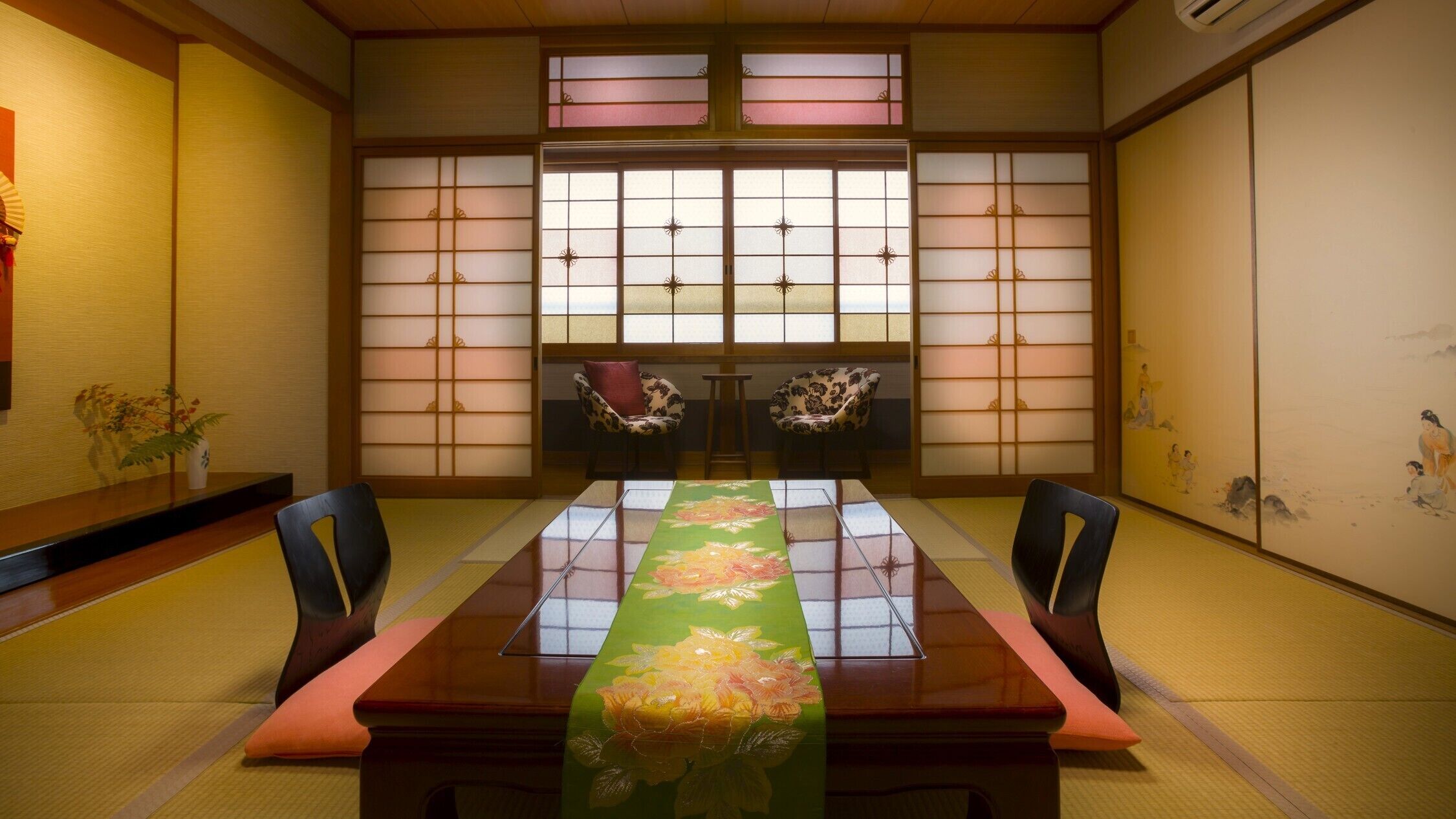 Habitació japonesa tradicional amb sòls de tatami, una taula baixa i un corredor floral verd, i portes corredisses amb un disseny de graella.