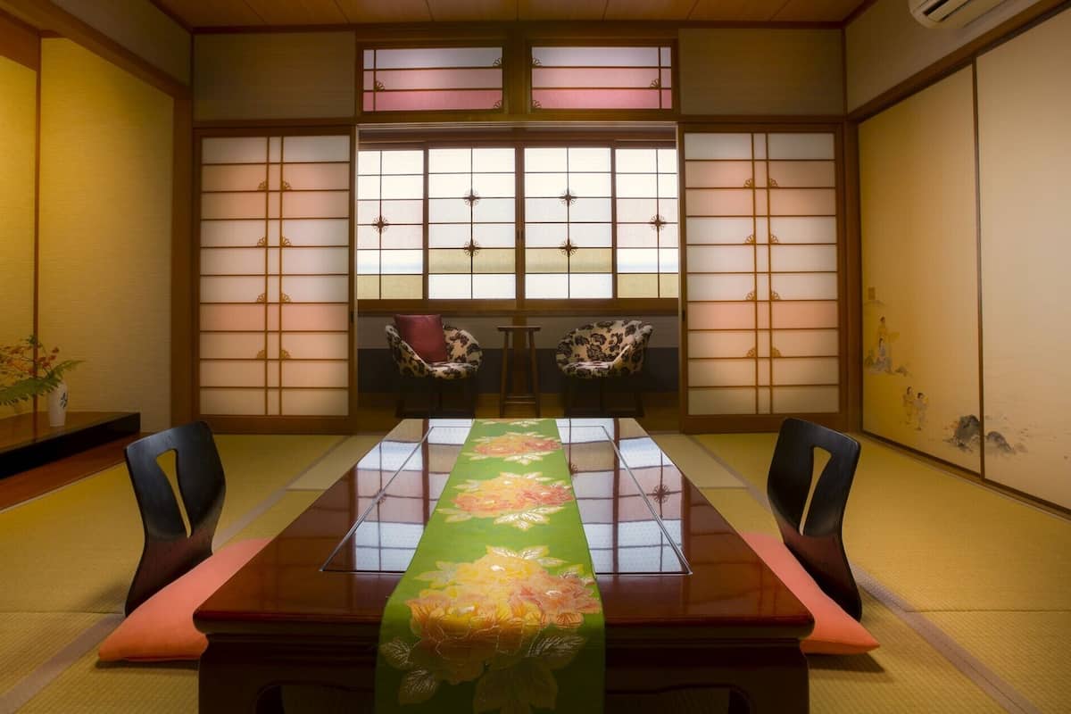 A traditional Japanese room with tatami flooring, a low table with a green floral table runner, and sliding doors with a grid pattern.