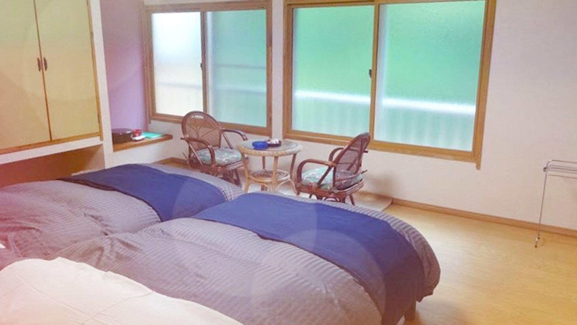 A bedroom with two beds, a small table, two chairs, and large windows.