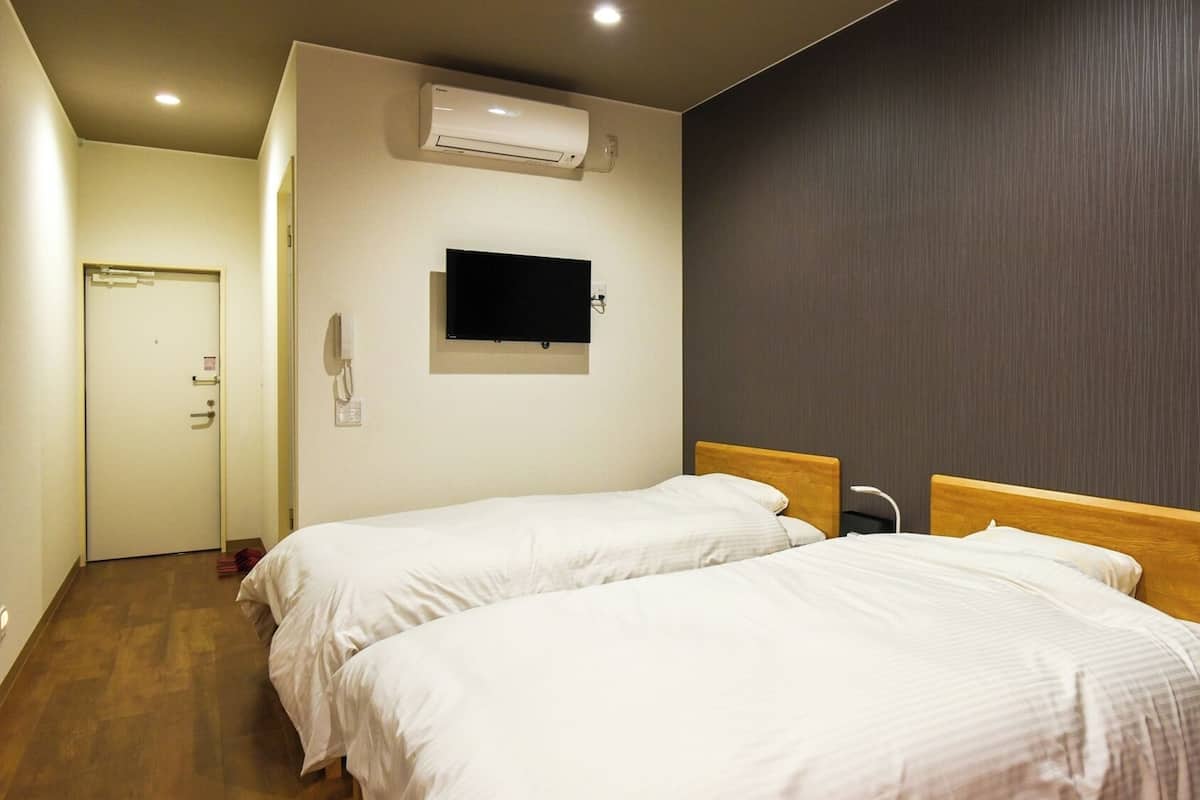 Ein Hotelzimmer mit zwei Betten, einem Flachbildfernseher, einer Klimaanlage und einer Tür.