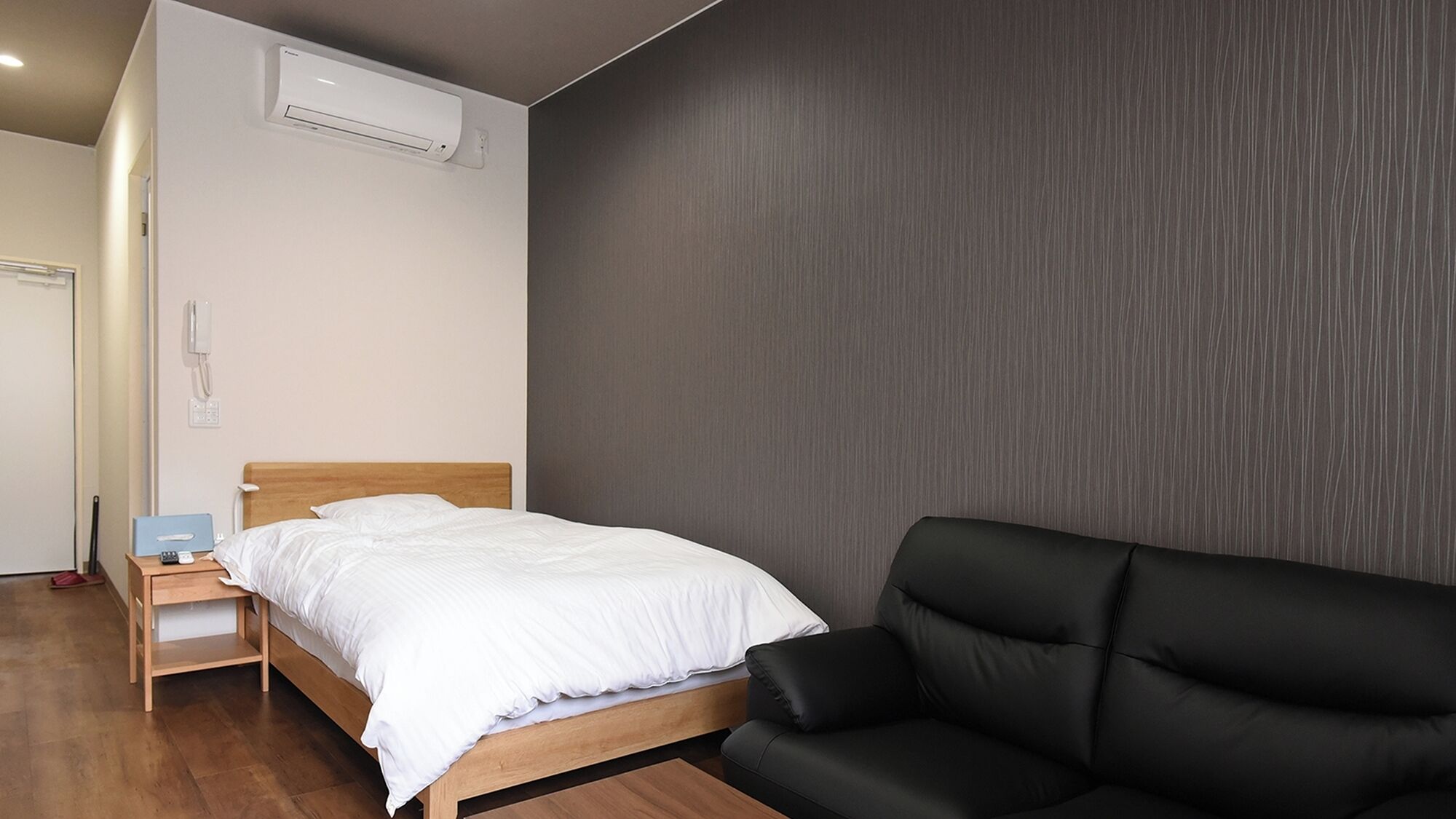 Ein Schlafzimmer mit einem Bett, einer schwarzen Couch, einem Nachttisch aus Holz, einem Telefon und einer Klimaanlage.