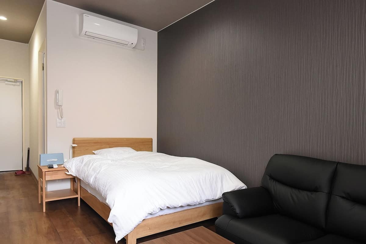 Ein Schlafzimmer mit einem Bett, einer schwarzen Couch, einem Nachttisch aus Holz, einem Telefon und einer Klimaanlage.