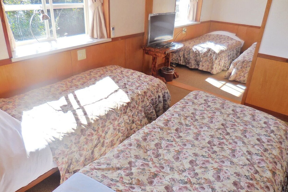 Ein Zimmer mit zwei Betten, einem Fernseher auf einem Holzschrank und einem Fenster mit Vorhängen.