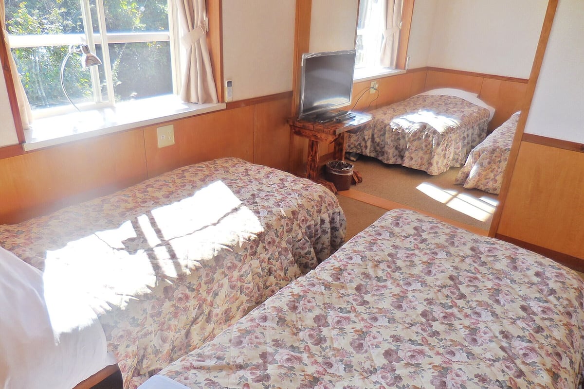 Ein Zimmer mit zwei Betten, einem Fernseher auf einem Holztisch und einem Fenster mit Vorhängen.