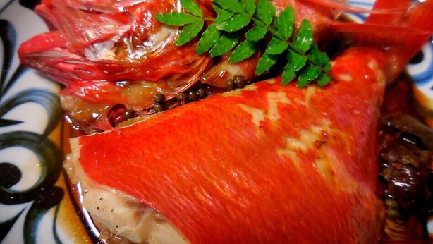 A close-up of a cooked fish with a garnish, served on a patterned plate. - Jogasaki Kawakami Pension (Ito)