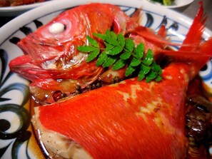 A close-up of a cooked fish with a garnish, served on a patterned plate. - Jogasaki Kawakami Pension (Ito)