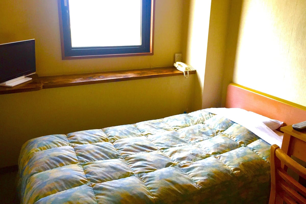 Ein Zimmer mit einem Bett, einem Fernseher auf einem Tisch, einem Fenster und einem Telefon auf einer Ablagefläche.