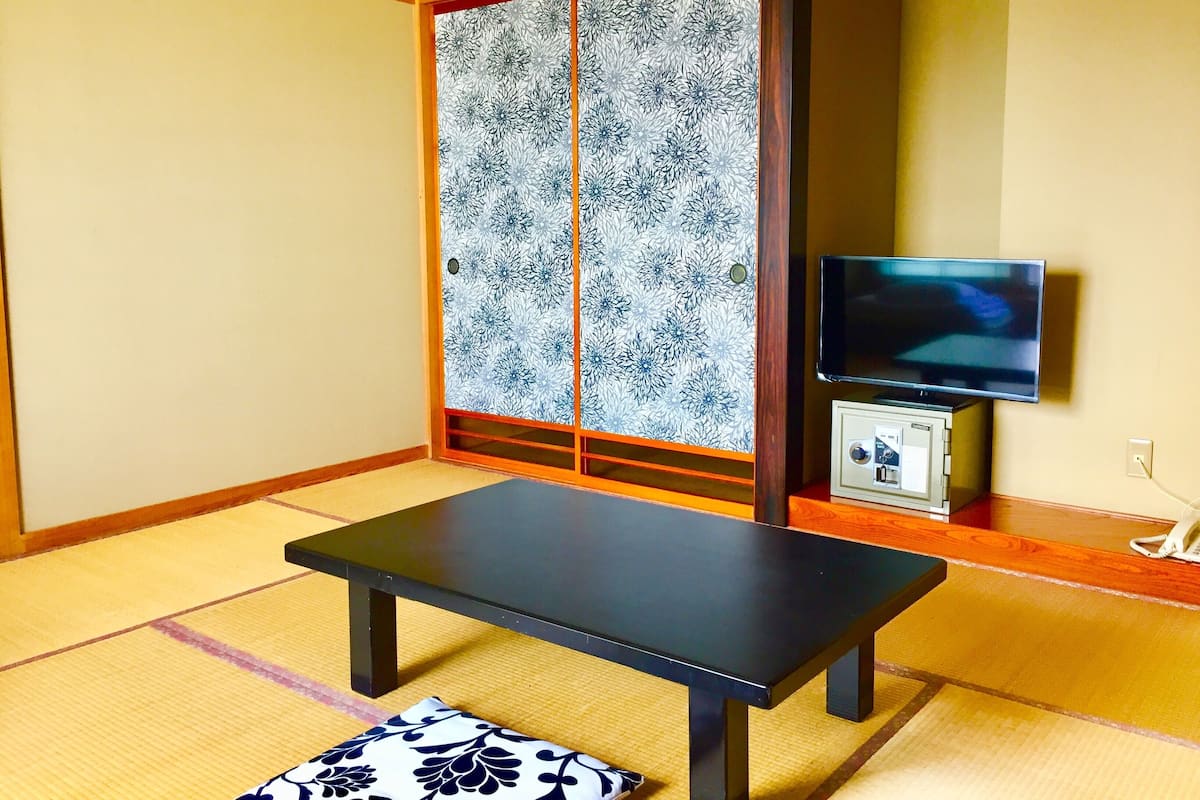 Ein Raum mit Tatami-Matten, einem niedrigen Tisch, einem Fernseher und einer traditionellen Schiebetür.