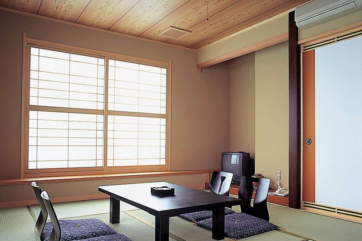 Ein traditioneller japanischer Raum mit Tatami-Boden, einem niedrigen Tisch, einem Fernseher und einer Schiebetür.