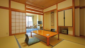 Ein traditioneller japanischer Raum mit Tatami-Boden, einem niedrigen Tisch, einem Fernseher und Schiebetüren.