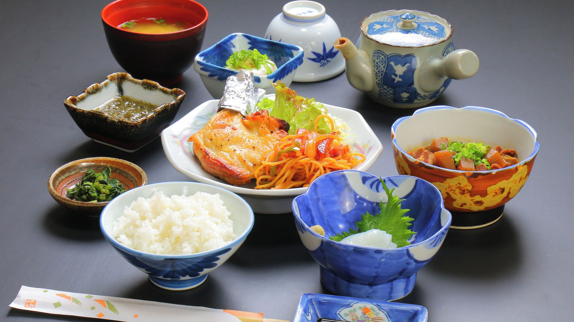 Japanilaisia ruokia ja perinteisiä teekulhoja ja -tarvikkeita on esillä pöydällä.