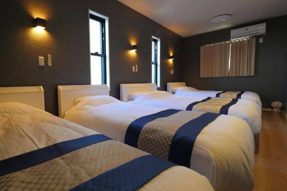 Une chambre d’hôtel avec trois lits, chacun doté d’une tête de lit, et deux appliques murales.