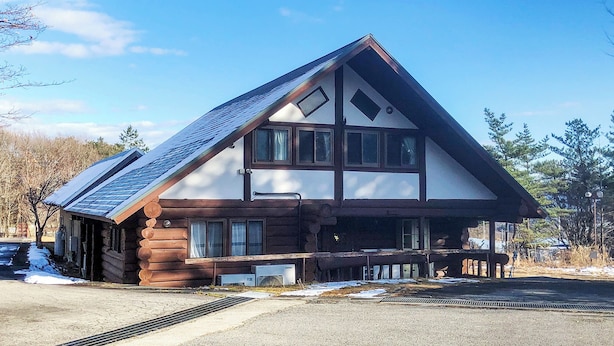 A log cabin with a steeply pitched roof, large windows, and a porch.