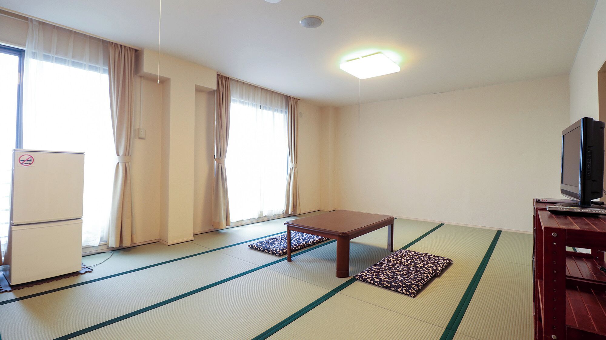 Ein Zimmer mit Tatami-Matten, einem kleinen Tisch, einem Fernseher und einem Kühlschrank.