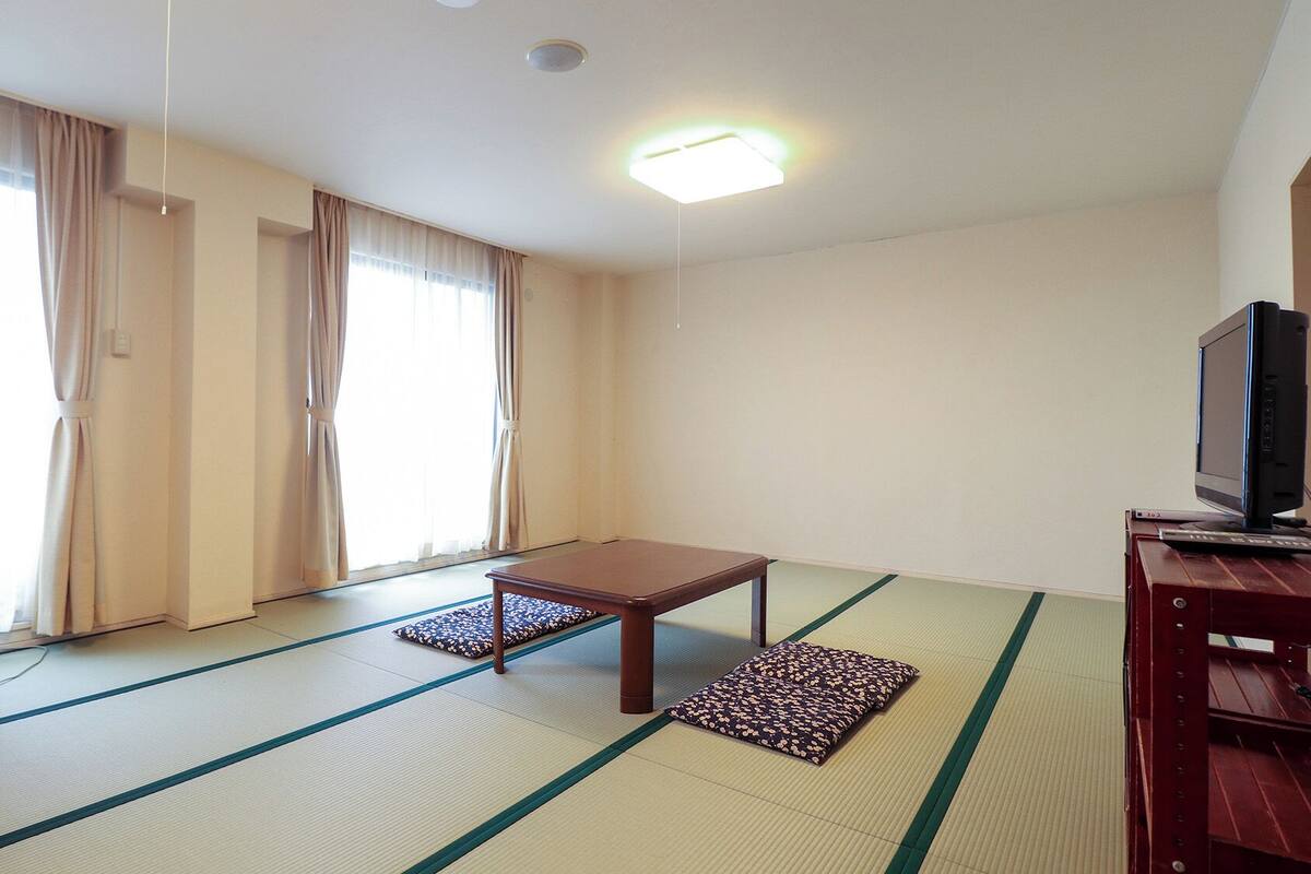 A room with tatami mats, a small table, a television, and a refrigerator.