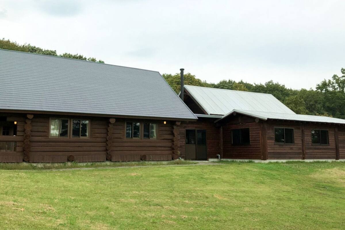 A log cabin with a large overhanging roof, a porch, and a grassy yard.