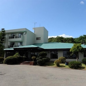 A two-story building with a green roof, a clock on the facade, and a well-maintained garden with bushes and a small tree. - Nasu Sports Garden (Nasu)