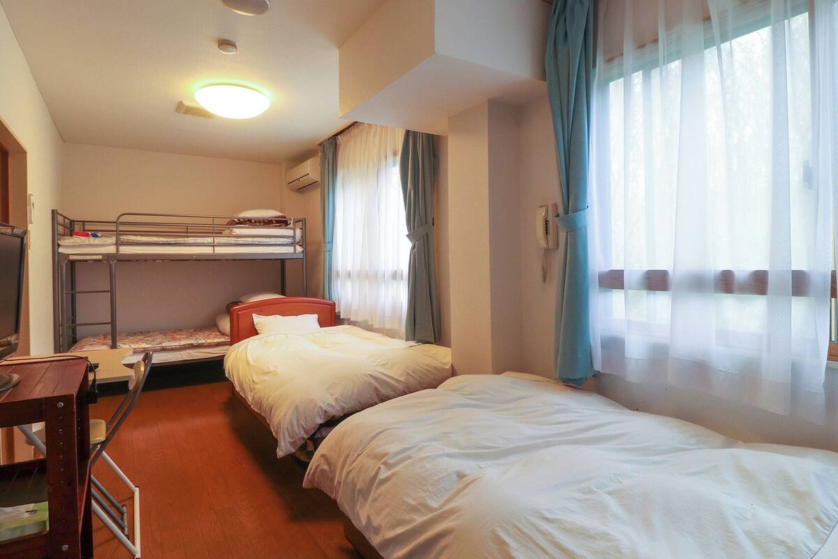 A hotel room with bunk beds, a desk with a computer, a telephone, and a window with curtains.
