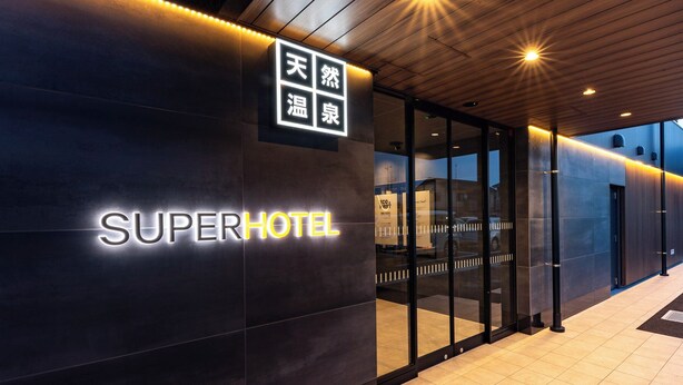 La entrada de un hotel con un letrero que dice 'SUPERHOTEL' y un letrero más pequeño con caracteres chinos.