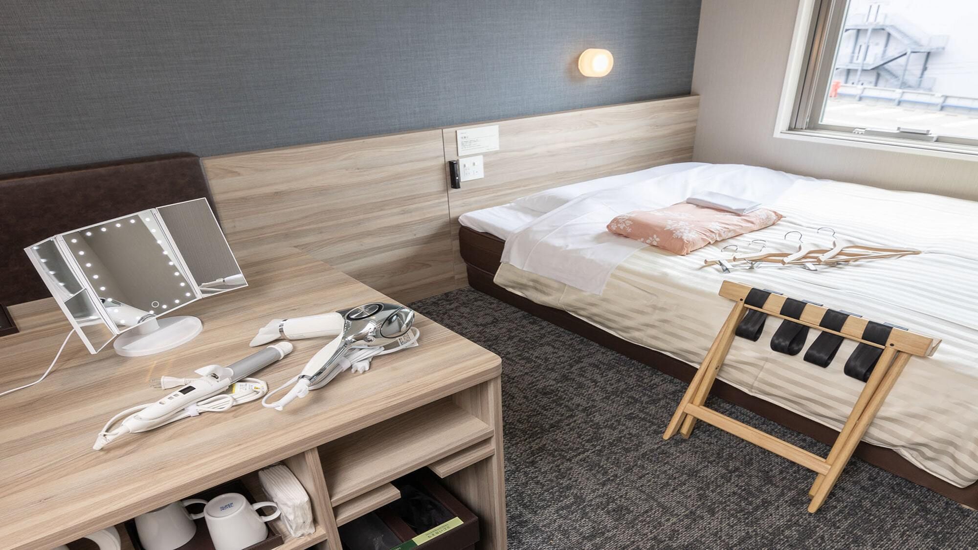 Quarto de hotel com cama, mesa de cabeceira, espelho e uma pequena cadeira de madeira.