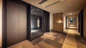 Un pasillo moderno de hotel con alfombra a cuadros, revestimiento de paneles de madera y un ascensor con pantalla digital.