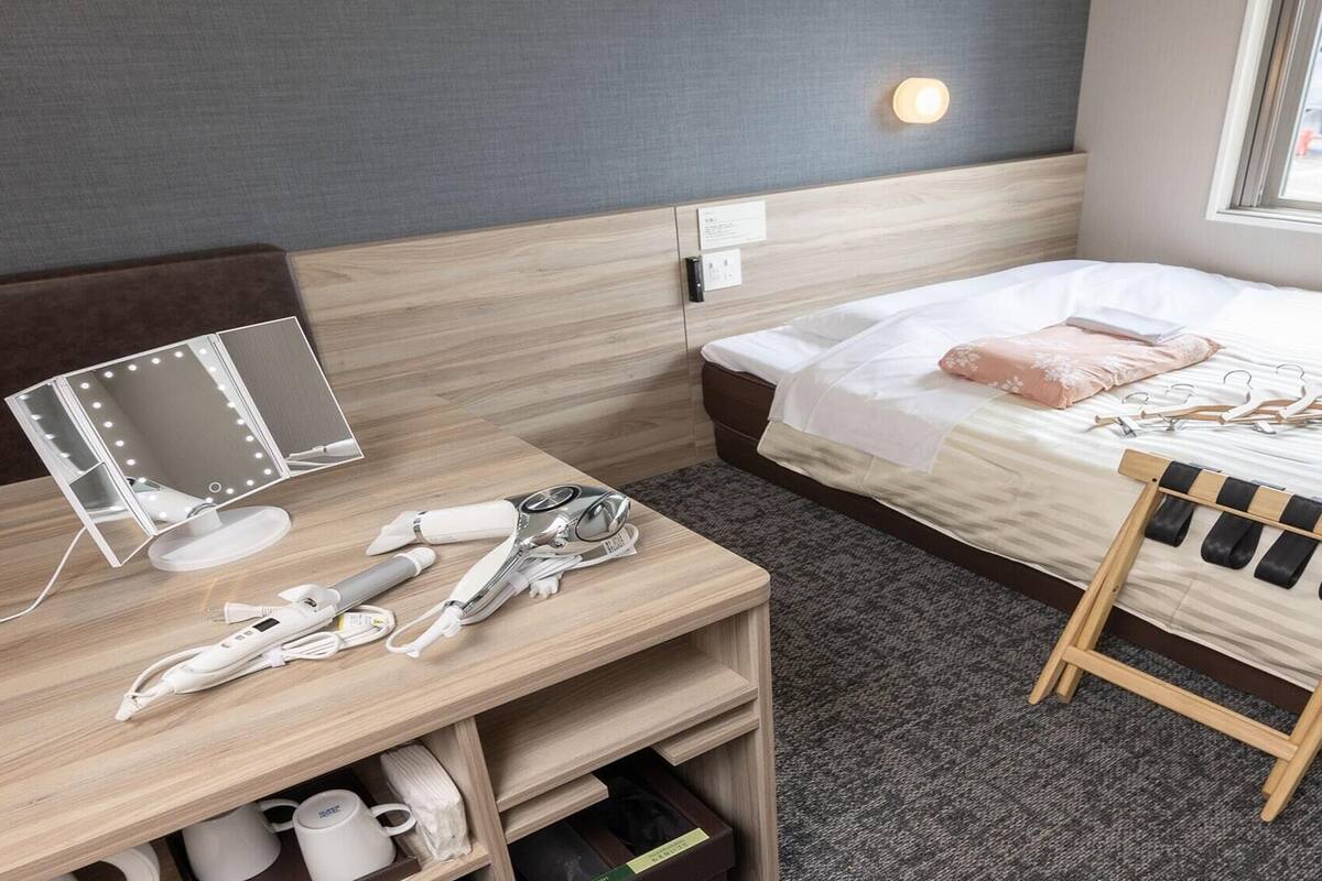 A hotel room with a bed, a bedside table with a mirror, a hairdryer, and a wooden hanger.
