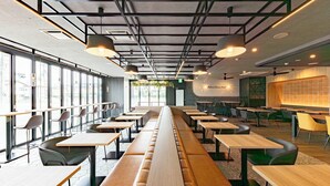 Un interior de restaurante moderno con mesas comunes largas, cabinas individuales y un techo alto con vigas a la vista.
