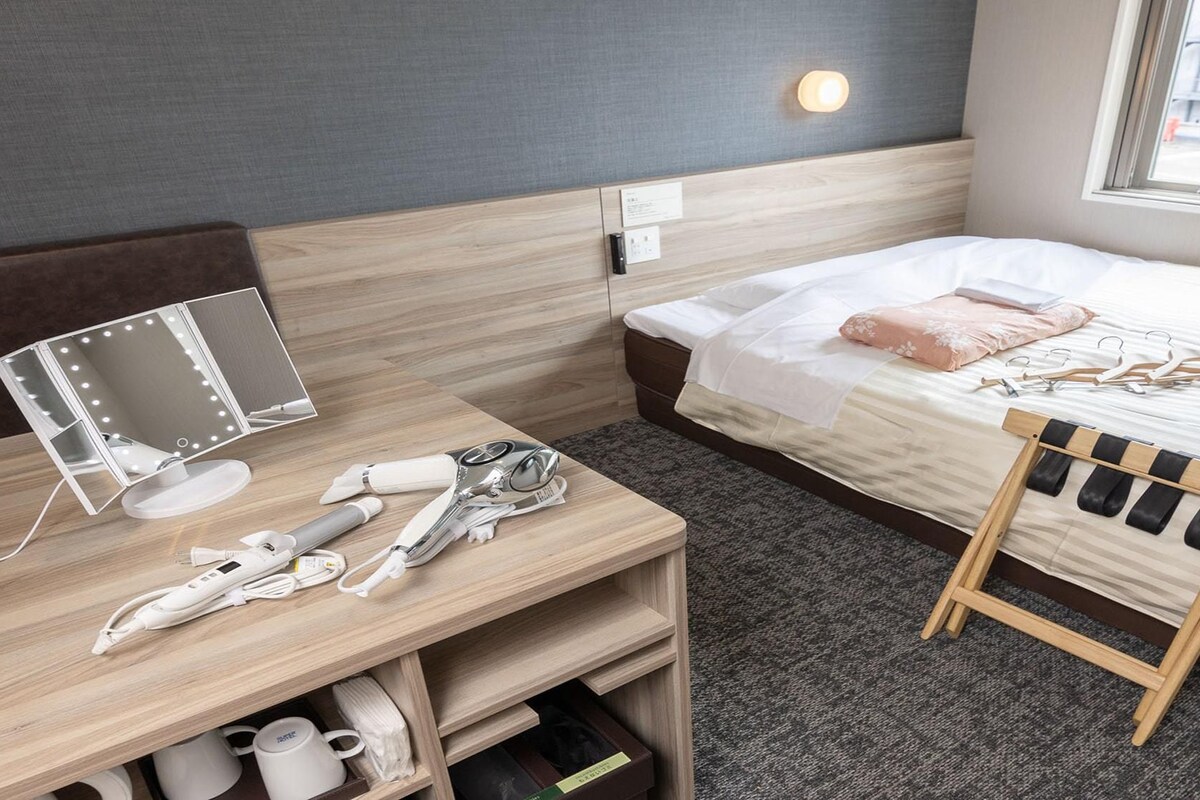 A hotel room with a bed, bedside table, mirror, and a small wooden chair.