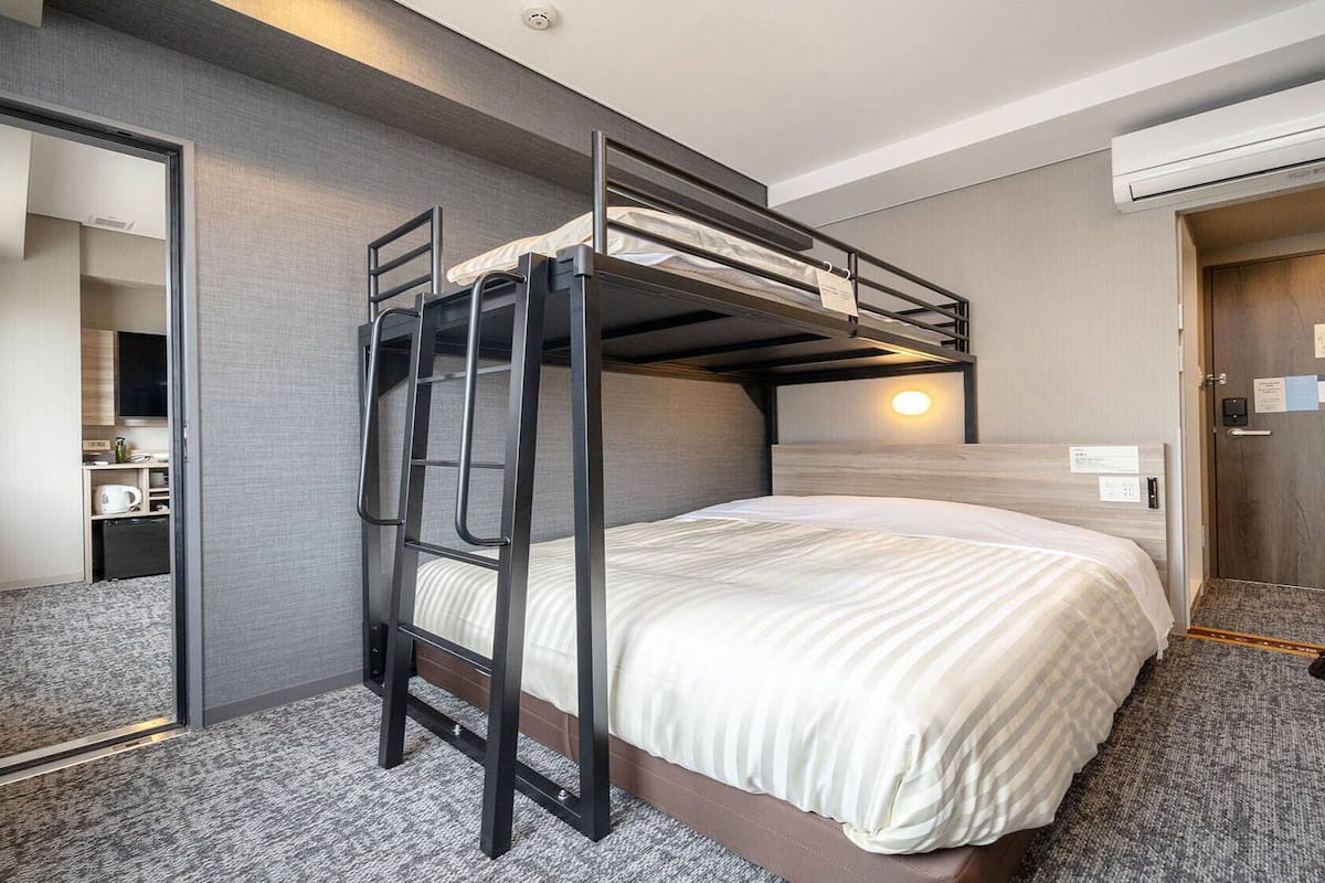 A bunk bed room with a mirror, a desk with a chair, and a wall-mounted light.